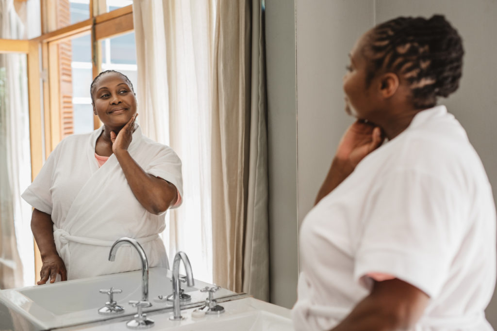 Woman wearing a bathrobe looking at her complexion in the mirror while standing in her bathroom in the morning