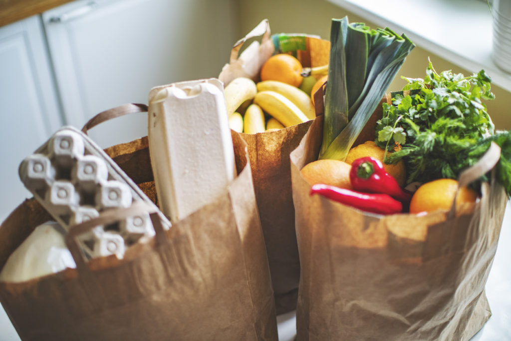 paper bags of groceries including eggs, fruit, leeks, and chiles