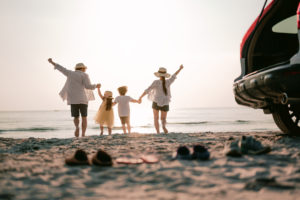 Happy family running on the beach in the sunset. Back view of a happy family on a tropical beach and a car on the side.