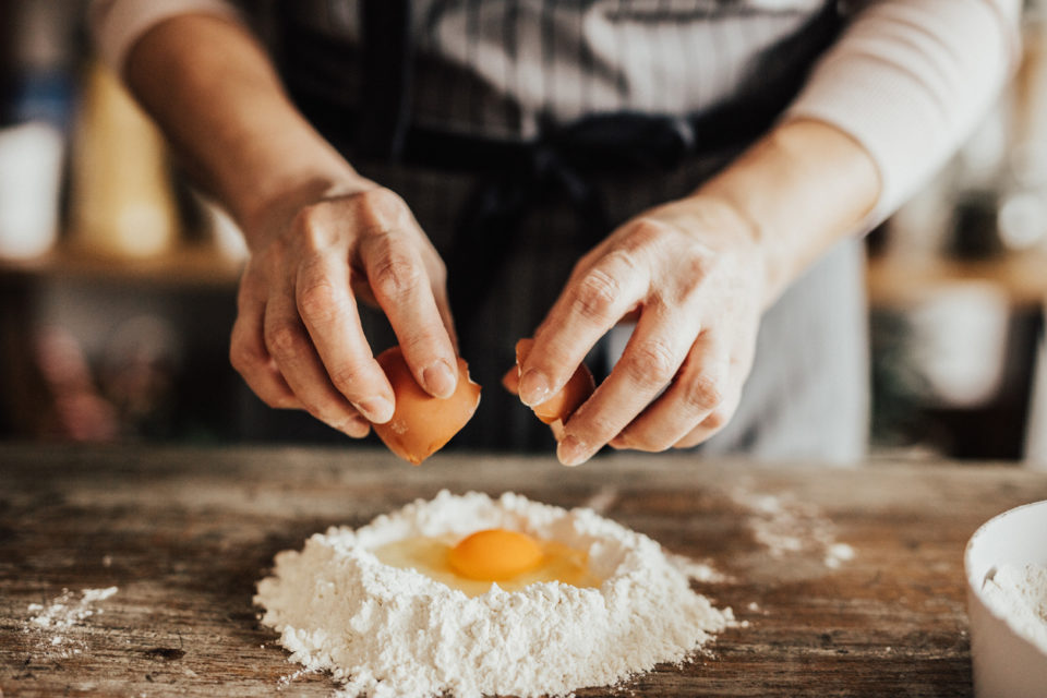 Woman adds an egg to the flour