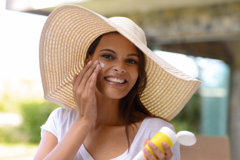 woman in hat applying sunscreen
