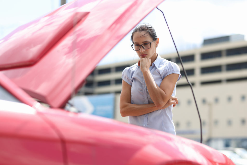 Pensive woman looks at car engine.