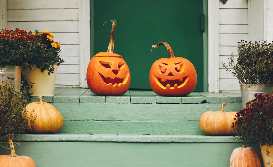 two jack-o-lanterns on a front porch that is painted green