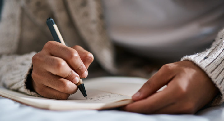 Cropped shot of a person writing in a notebook on their bed