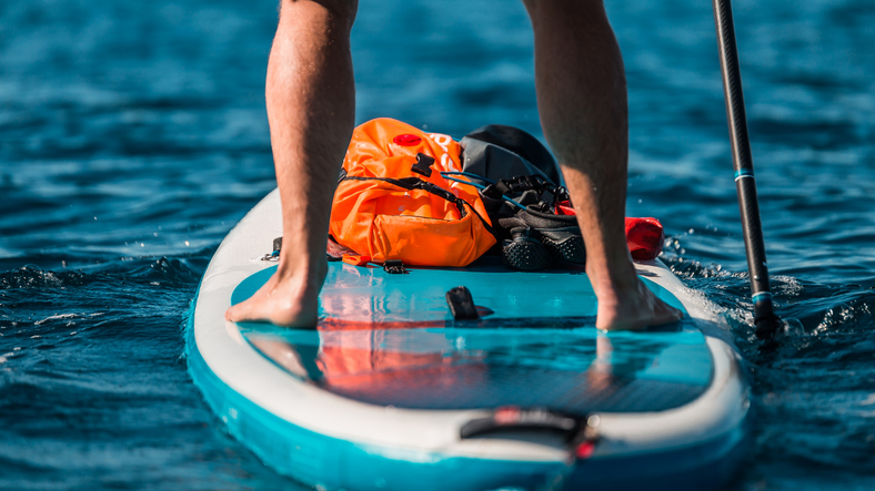 Young athletic man paddling on a SUP stand up paddle board in blue water